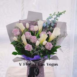 Arrangement of lavender roses, white tulips, and calla lilies in wrapped bouquet with purple accents