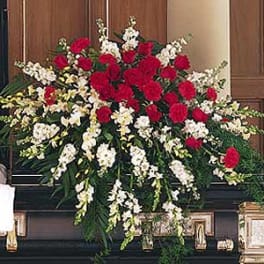 Red and white casket spray with red carnations and white flowers on a dark casket