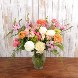 Tall mixed arrangement of pink, peach, and white flowers in a textured green glass vase