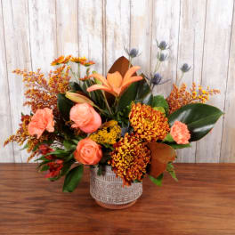 Autumn-toned arrangement with orange roses, lilies, and mums in a patterned ceramic vase