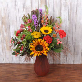 Mixed bouquet with sunflowers, carnations, and purple blooms in a red vase