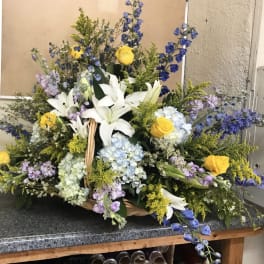 Large basket arrangement with white lilies, yellow roses, blue hydrangeas, and purple flowers
