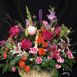 Basket arrangement of pink roses, orange roses, lilies, and a birthday topper