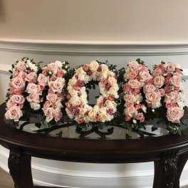 Floral arrangement spelling "MOM" with pink and cream roses