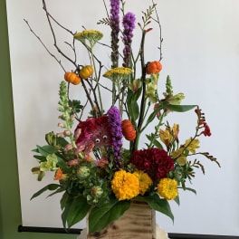 Tall mixed floral arrangement in a wooden box with orange accents