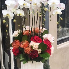 Tall floral arrangement with white orchids and red roses in a white vase