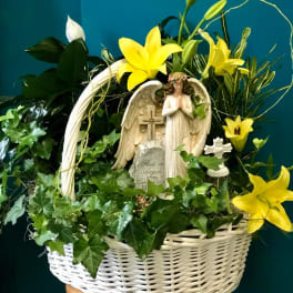 White basket arrangement with yellow lilies and an angel statue