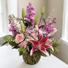 Pink lilies and roses in a glass vase with purple flowers