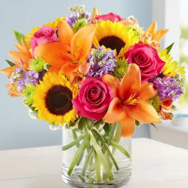 Bright mixed bouquet of roses, lilies, and sunflowers in a glass vase