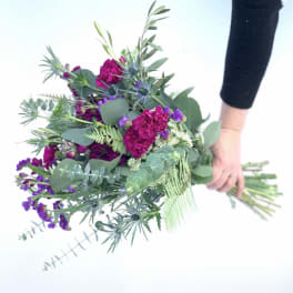 Handheld bouquet of magenta and purple flowers with mixed greenery