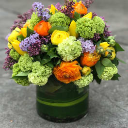 Bright mixed bouquet in a green glass vase with orange, yellow, purple, and green blooms