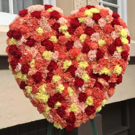 Heart-shaped floral arrangement of red, pink, peach, and yellow carnations