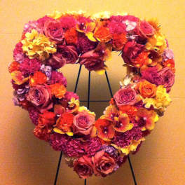 Heart-shaped floral wreath with pink, red, and yellow blooms on a stand