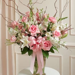 Pink roses and white lilies in a clear glass vase with a pink ribbon