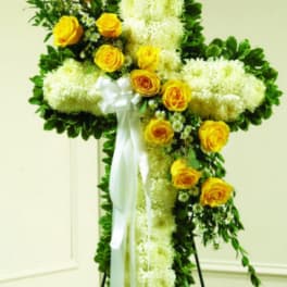 Yellow roses and white flowers arranged in a cross on a stand with a white ribbon