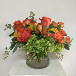 Orange roses and green hydrangeas in a clear glass vase