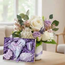 Bouquet of white and lavender roses in a striped vase with a purple gift box