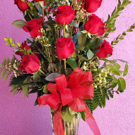 Red roses arranged in a clear glass vase with a red ribbon bow
