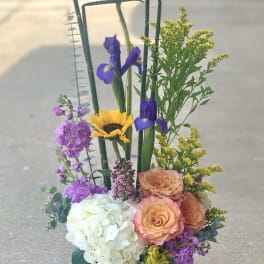 Mixed floral arrangement in a green vase with sunflowers, irises, roses, and hydrangea