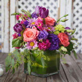 Colorful bouquet of roses, tulips, and daisies in a square glass vase