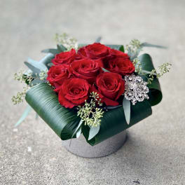 Red roses arranged in a low box with a jeweled brooch accent