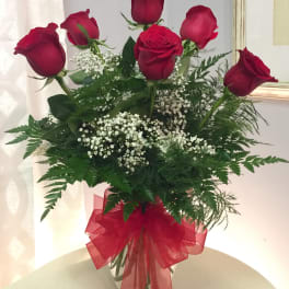 Red roses in a clear vase with baby's breath and a red ribbon