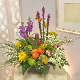 Mixed floral arrangement in a rectangular container with purple, yellow, orange, pink, and white blooms