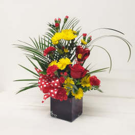 Red and yellow flower arrangement in a black vase with a polka-dot ribbon and heart balloon