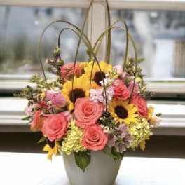 Basket arrangement of pink roses and yellow sunflowers in a gray container