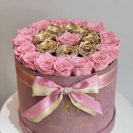 Pink and gold roses arranged in a round hat box with a ribbon bow