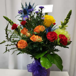 Mixed bouquet of roses, carnations, and blue thistle in a purple vase