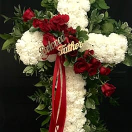 Cross-shaped floral tribute with white blooms and red roses on a black stand