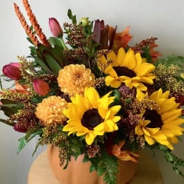 Autumn bouquet with sunflowers, tulips, and orange blooms in a pumpkin-colored vase.