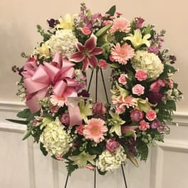 Heart-shaped floral wreath with pink ribbon and mixed pastel flowers on an easel