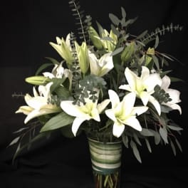 White lilies arranged in a clear glass vase with eucalyptus foliage