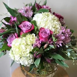 Bouquet of pink roses, white hydrangeas, and purple flowers in a glass vase