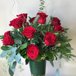 Red roses arranged in a clear glass vase with greenery