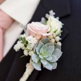 Boutonniere with pink and white roses and a succulent on a dark suit