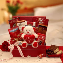 Red gift box with chocolates and a teddy bear holding a heart