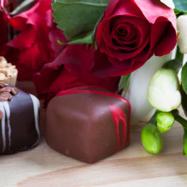 Red roses with assorted chocolates on a wooden surface