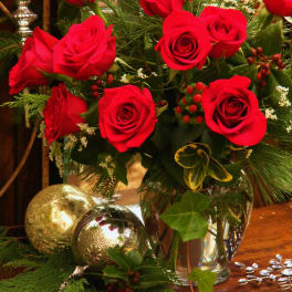 Red roses arranged in a clear glass vase with evergreen accents