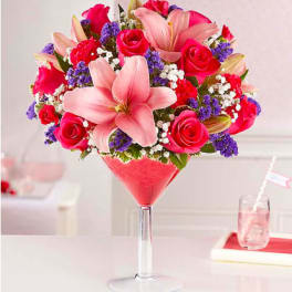 Pink lilies and roses arranged in a tall martini glass vase