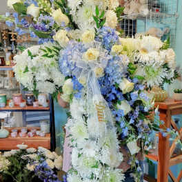 Tall white and blue floral cross spray with yellow roses and a ribbon reading Dad