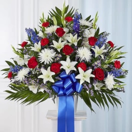 Large standing spray of red, white, and blue flowers with a blue ribbon