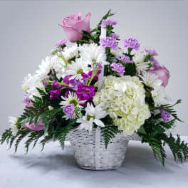 Pink roses, white daisies, and purple flowers in a white basket