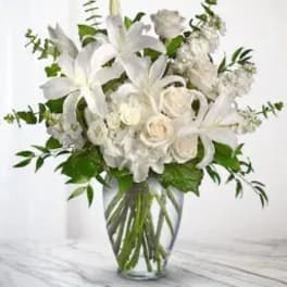 White lilies and roses in a clear glass vase with greenery