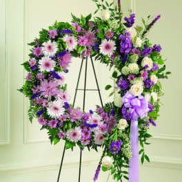 Purple and white floral wreath on a stand with a lavender ribbon