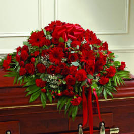 Red floral casket spray with ribbon on a wooden coffin