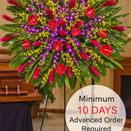 Large round tropical standing spray with red, purple, and yellow flowers on a metal easel in a funeral setting