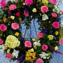 Large floral wreath on a stand with pink, yellow, white, and purple blooms